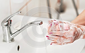 Young woman washing her hands under water tap faucet with soap. Detail on fingers, nails covered purple polish. Personal hygiene