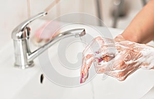 Young woman washing her hands under water tap faucet with soap. Detail on suds covered skin. Personal hygiene concept -