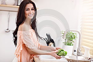 Young woman washing lettuce in modern kitchen