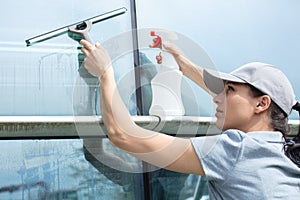 Young woman washing window with squeegee