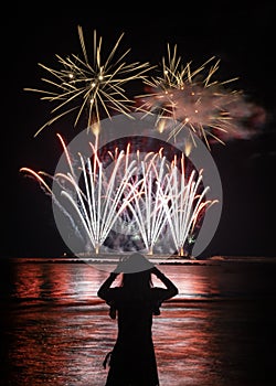 Young woman watches fireworks by the sea