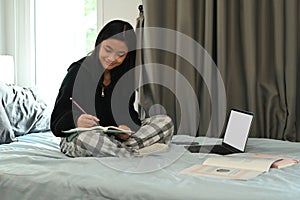 Young woman watching learning online in virtual classroom on laptop while sitting in bedroom. E-learning education