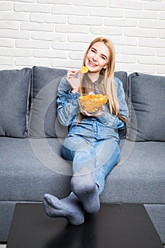 Young woman watching TV and eating chips on sofa