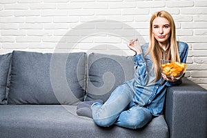 Young woman watching TV and eating chips on sofa