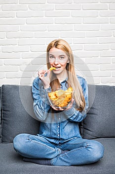 Young woman watching TV and eating chips on sofa at home