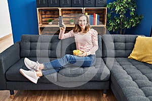 Young woman watching tv holding tv remote control at home