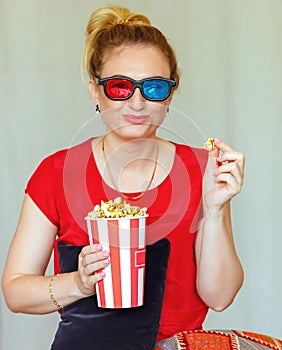 Young woman watching tv while sitting on a sofa with 3d glasses and popcorn with pleasure