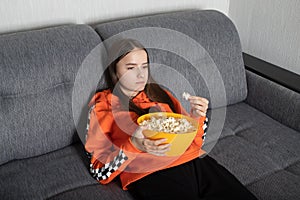 Young woman watching an uninteresting show on TV with popcorn in her hands