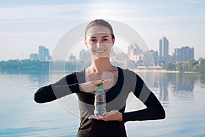 Young woman with water bottle at river and city backround