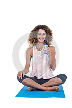 Young woman with water bottle sitting on exercise mat