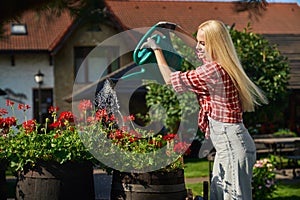 Young woman watering beautiful flowers on back yard