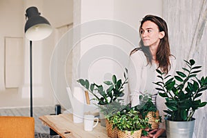 Young woman watering flowerpots at home. Casual lifestyle series in modern scandinavian interior