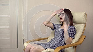 A young woman waves her hands because she is hot. A woman in a stuffy room sits on a chair.