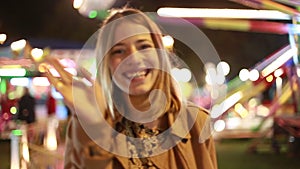Young woman waving and beckoning to camera in amusement park