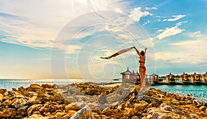 Young woman waving scarf in wind at beach. Happy woman in red bikini holding tissue and looking away at sea.