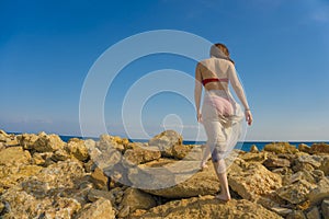 Young woman waving scarf in wind at beach. Happy woman in red bikini holding tissue and looking away at sea.