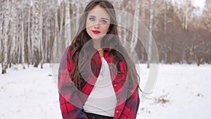 Young woman with wavy hair standing and touching face in winter forest