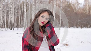 Young woman with wavy hair standing and touching face in winter forest