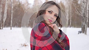 Young woman with wavy hair standing and touching face in winter forest