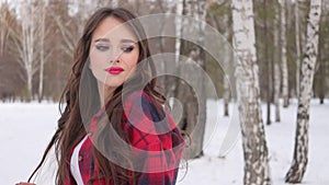 Young woman with wavy hair standing and touching face in winter forest