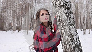 Young woman with wavy hair standing and touching face in winter forest