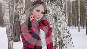 Young woman with wavy hair standing and touching face in winter forest