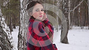 Young woman with wavy hair standing and touching face in winter forest