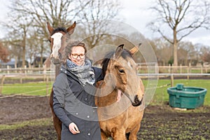 Young woman in a wax coat with her two 1 year old stallions in the pasture. Two curious horses heads