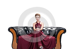 Young woman wear red dress fashion posing and sitting on black sofa looking at camera on isolated white background.