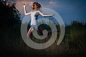 Young woman wearied denim shorts and tank top is running fust of dancing in tall grass in dark
