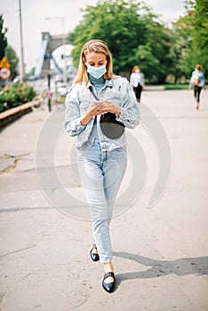 Young woman wearing antibacterial mask using phone in a city.