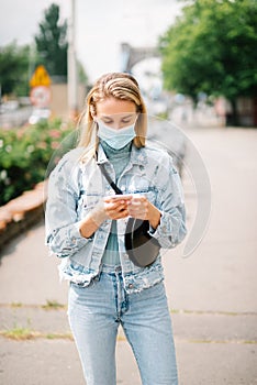 Young woman wearing antibacterial mask using phone in a city.