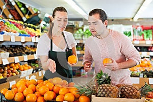 Young woman wearing apron selling fresh oranges to man customer