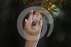 Young woman wearing beautiful silver ring with prehnite gemstone near pine