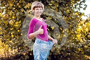 Young woman wearing big loose jeans with apple in hand - weight