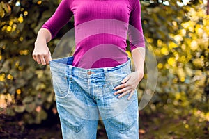 Young woman wearing big loose jeans with apple in hand - weight