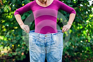 Young woman wearing big loose jeans with apple in hand - weight