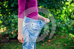 Young woman wearing big loose jeans with apple in hand - weight