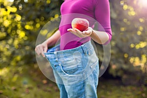 Young woman wearing big loose jeans with apple in hand - weight