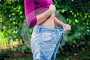 Young woman wearing big loose jeans with apple in hand - weight