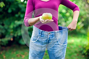 Young woman wearing big loose jeans with apple in hand - weight