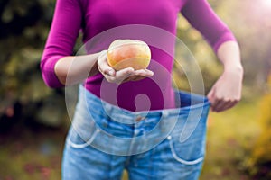 Young woman wearing big loose jeans with apple in hand - weight