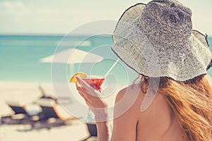 Young woman wearing a bikini holding a cocktail enjoying ocean view