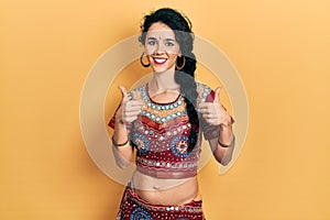 Young woman wearing bindi and bollywood clothing success sign doing positive gesture with hand, thumbs up smiling and happy