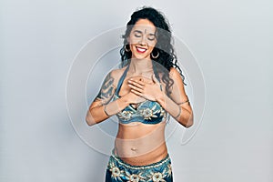 Young woman wearing bindi and traditional belly dance clothes smiling with hands on chest with closed eyes and grateful gesture on