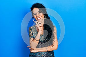 Young woman wearing bindi and traditional kurta dress looking confident at the camera with smile with crossed arms and hand raised