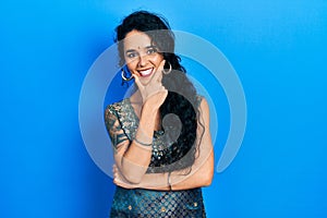 Young woman wearing bindi and traditional kurta dress looking confident at the camera smiling with crossed arms and hand raised on