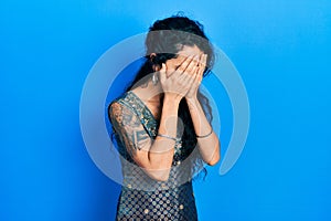 Young woman wearing bindi and traditional kurta dress with sad expression covering face with hands while crying