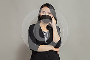 Young woman wearing black mask while folding one hand and holding right cheek