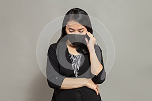 Young woman wearing a black mask holding her right cheek while lowering her head